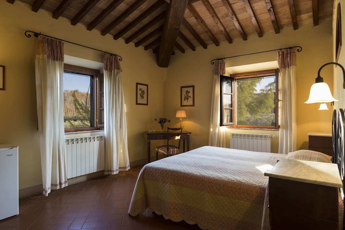 Une chambre à coucher avec un lit, un bureau, une chaise, une lampe et une fenêtre avec des rideaux.