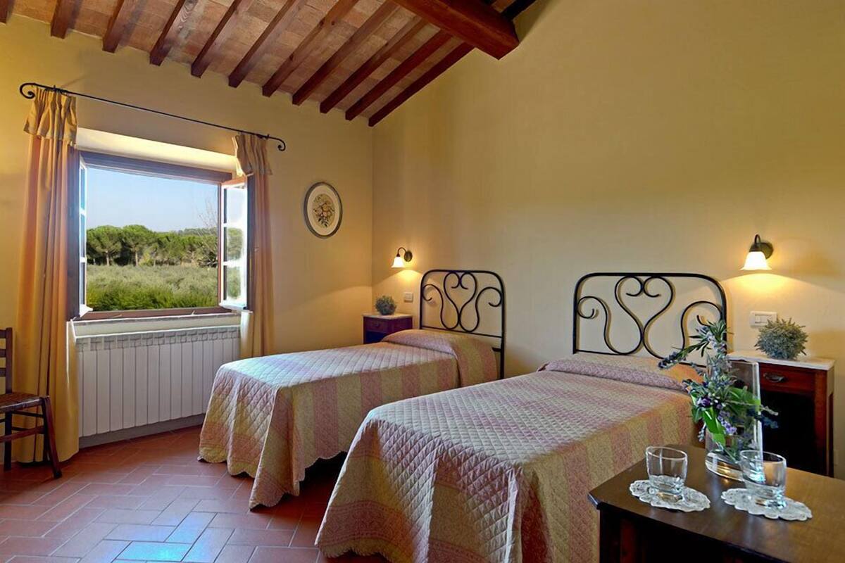 Une chambre avec deux lits, une fenêtre avec des rideaux, un radiateur, une petite table avec des verres et un luminaire fixé au mur.