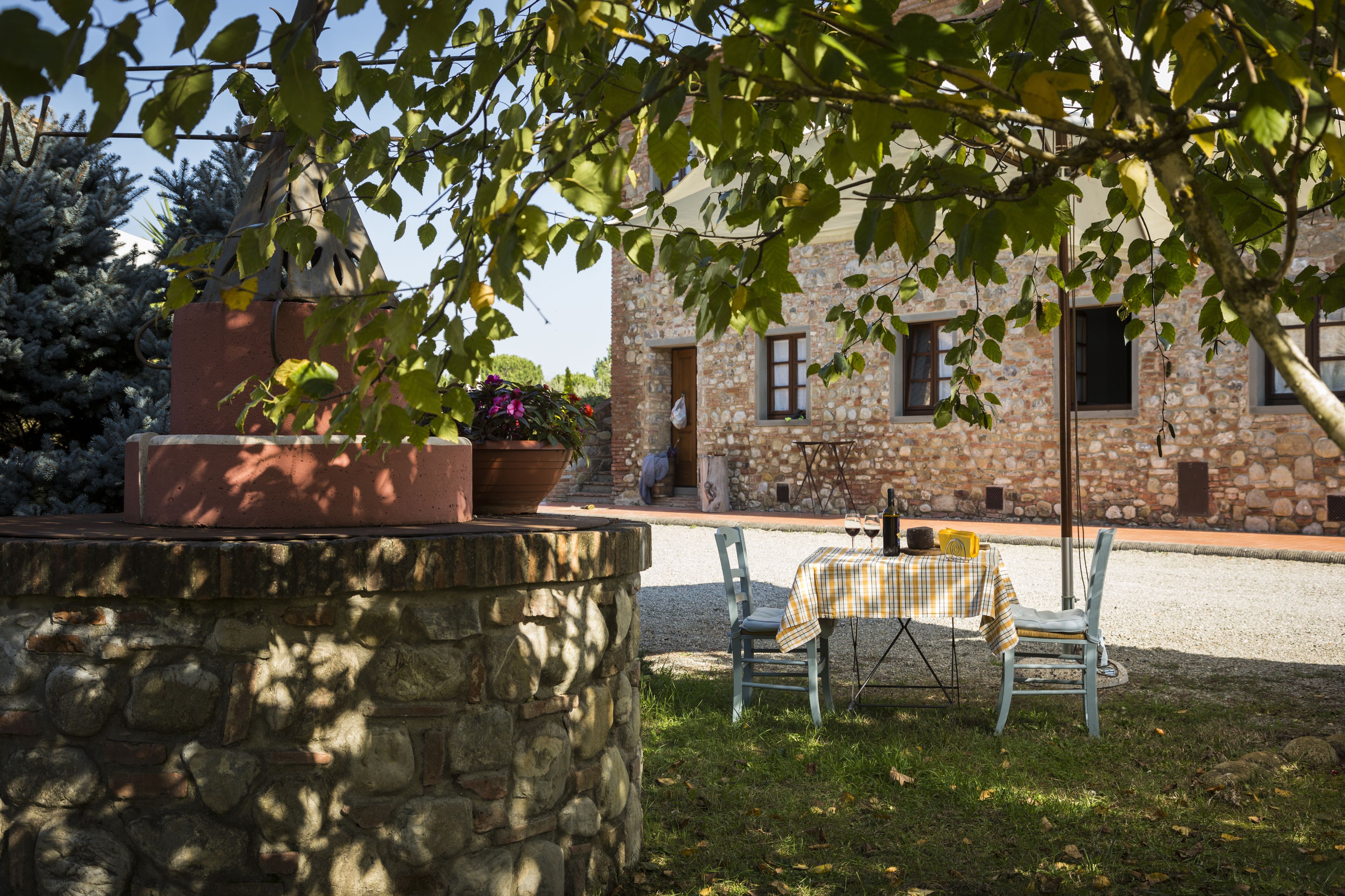 A stone building with a garden area featuring a table and chairs, a stone wall, and potted plants.