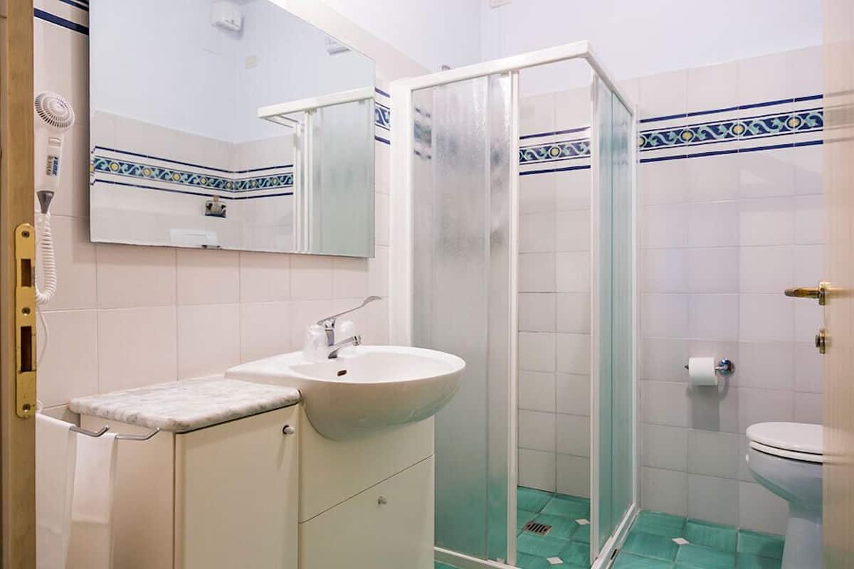 Une salle de bain avec un lavabo blanc, un miroir, un espace douche et des toilettes.