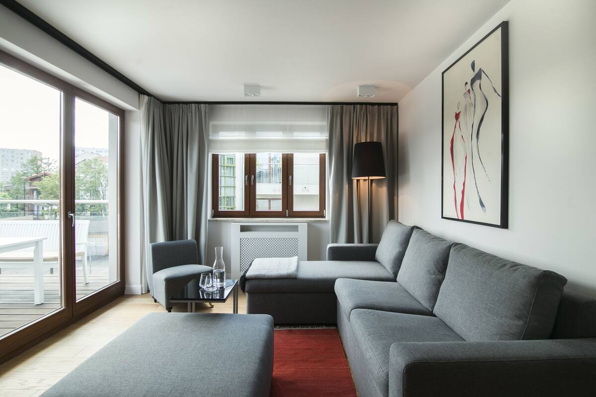 Una habitación de hotel moderna con un sofá gris, una mesita con un vaso y vistas al exterior a través de amplias ventanas.