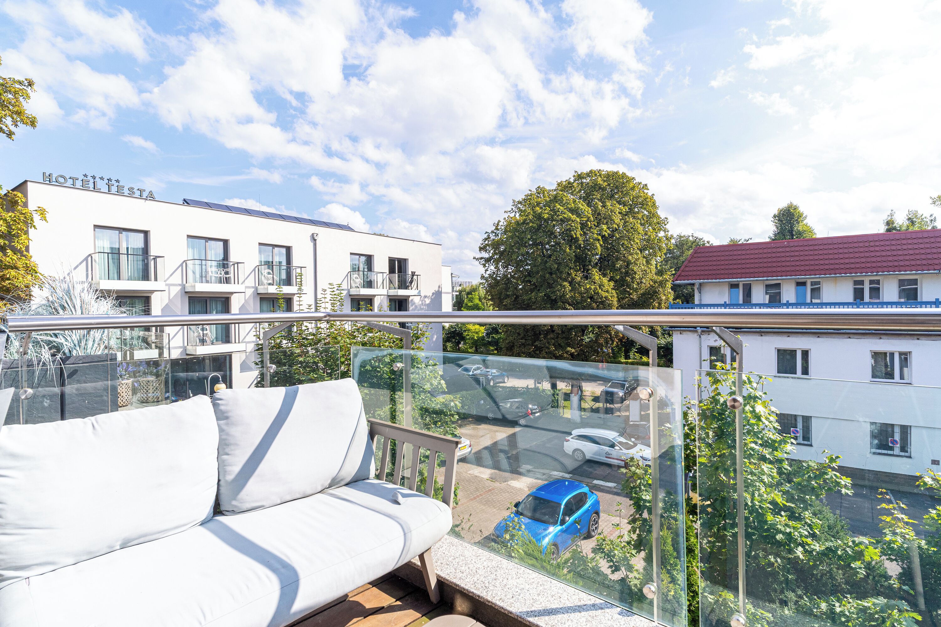 Ein Balkon mit einer weißen Couch, einer Glastrennwand und Blick auf eine Straße mit Autos und Gebäuden.