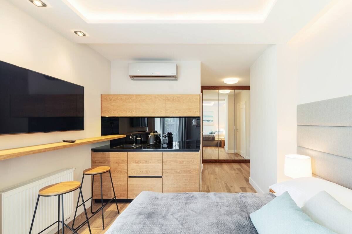 Una habitación de hotel moderna con kitchenette, una cama grande, televisión y vista al pasillo.