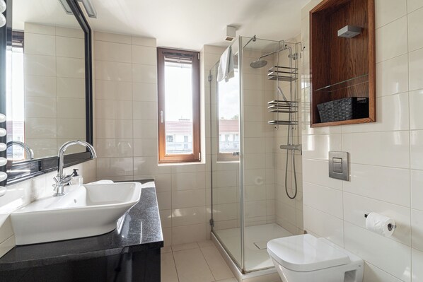 A modern bathroom with a glass-enclosed shower, a white sink, and a toilet.
