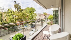 Ein Balkon mit Glastrennwand, einem weißen Stuhl, einem kleinen Tisch und einem Blumentopf.