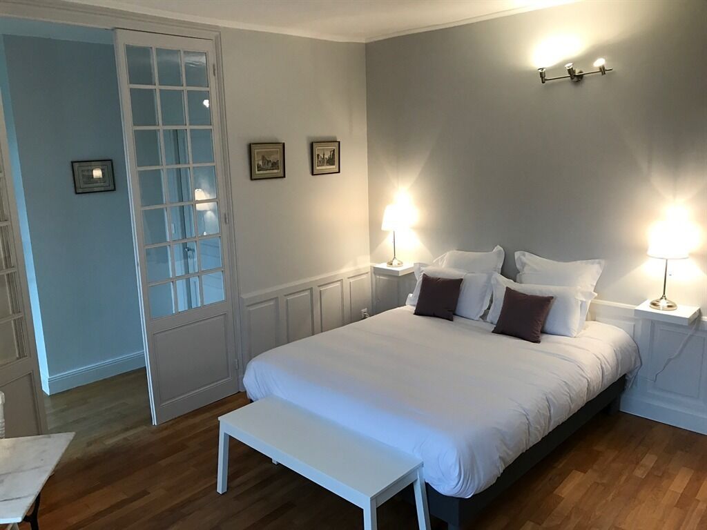 Een slaapkamer met een groot bed, nachtlampjes, een bankje en een deur met glaspanelen.