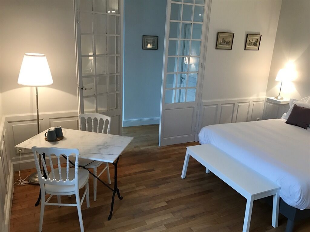 A room with a bed, a table, and a chair. There is a door with glass panels and a picture on the wall.
