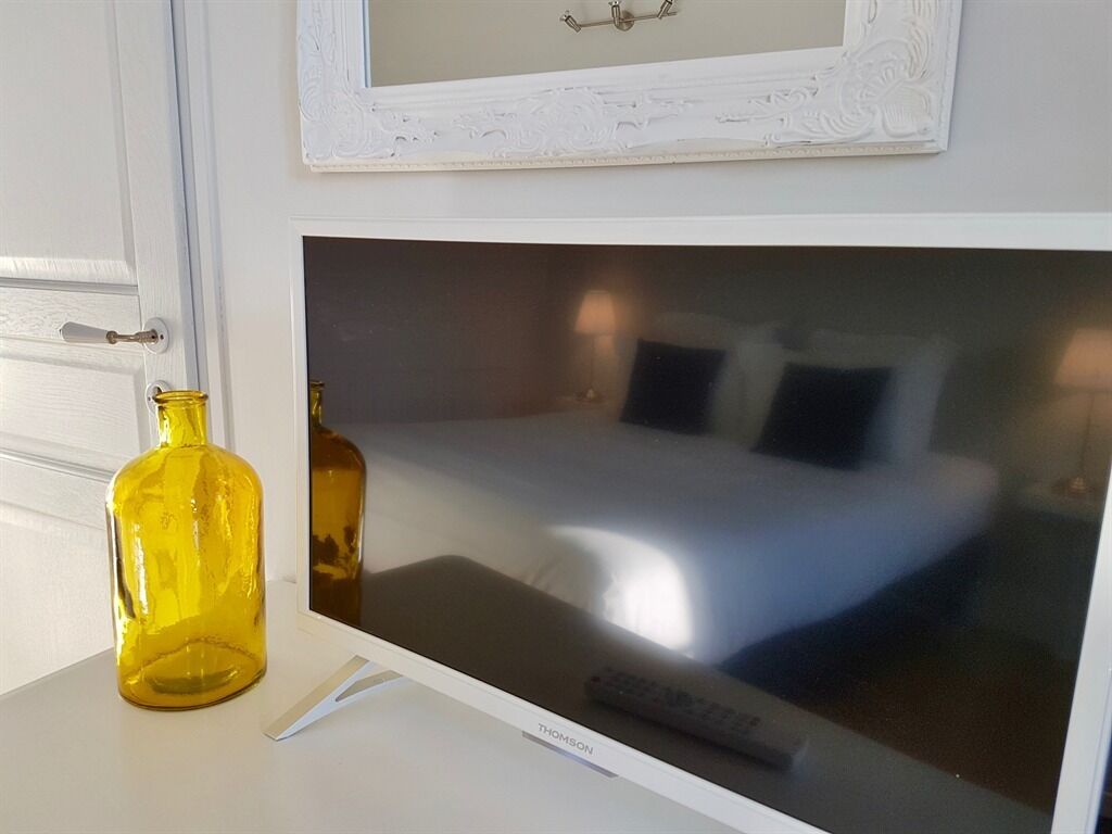 A hotel room with a bed, a TV, and a white wall with a decorative mirror.