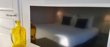 Habitación de hotel con cama, televisión y pared blanca con espejo decorativo.