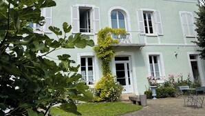 A two-story building with white shutters, a balcony, and a garden area.