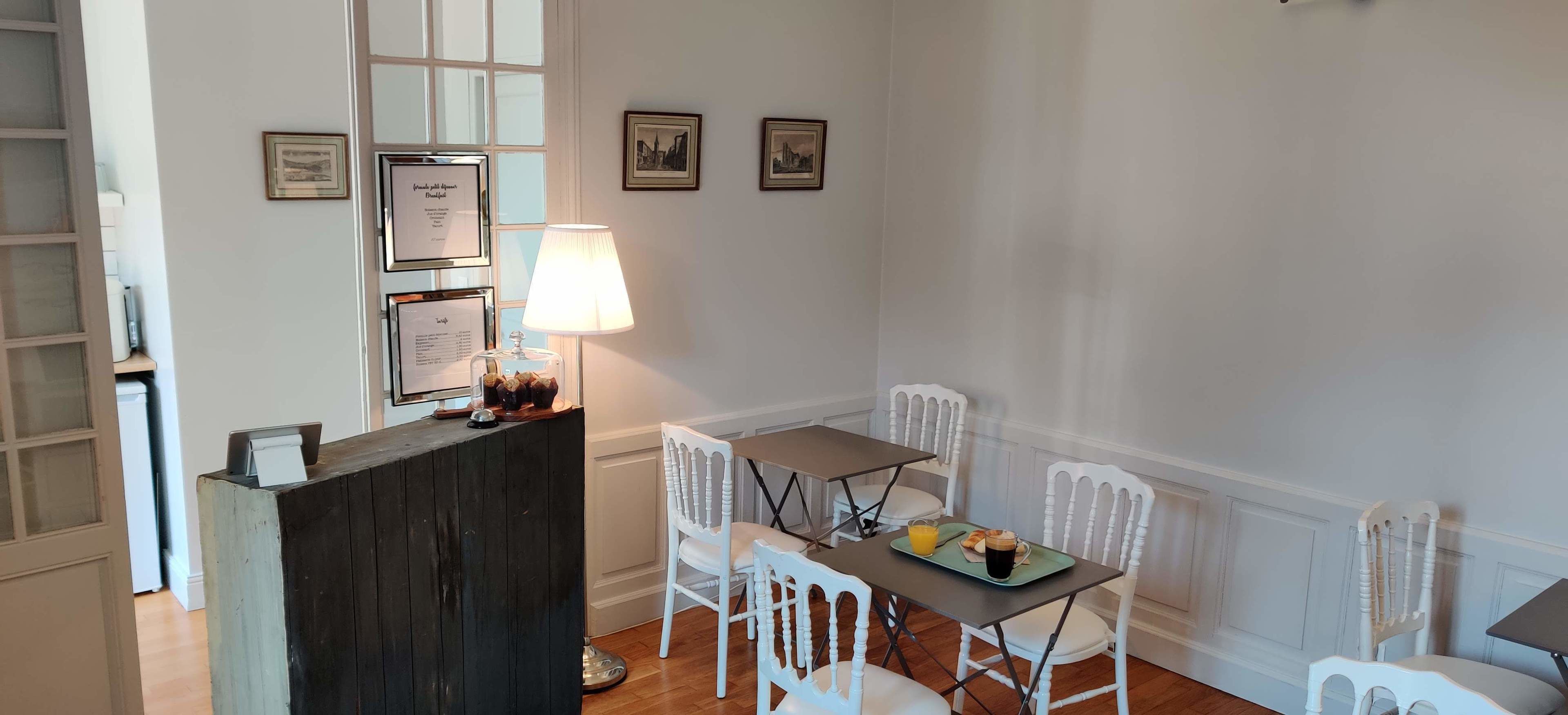 Un comedor con mostrador de madera, sillas blancas, una mesa con alimentos para el desayuno y certificados enmarcados en la pared.