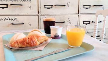 A breakfast tray with croissants, a glass of orange juice, and a cup of yogurt on a table with a vintage-style cabinet in the background.