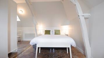 Un dormitorio con cama blanca, suelo de piedra, paredes blancas y vigas de madera a la vista.