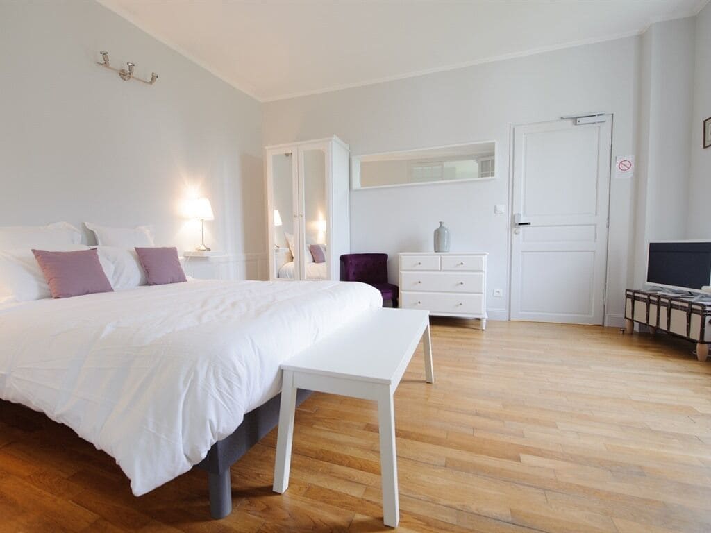 A bedroom with a bed, bedside tables, a dresser, a mirror, and a television.