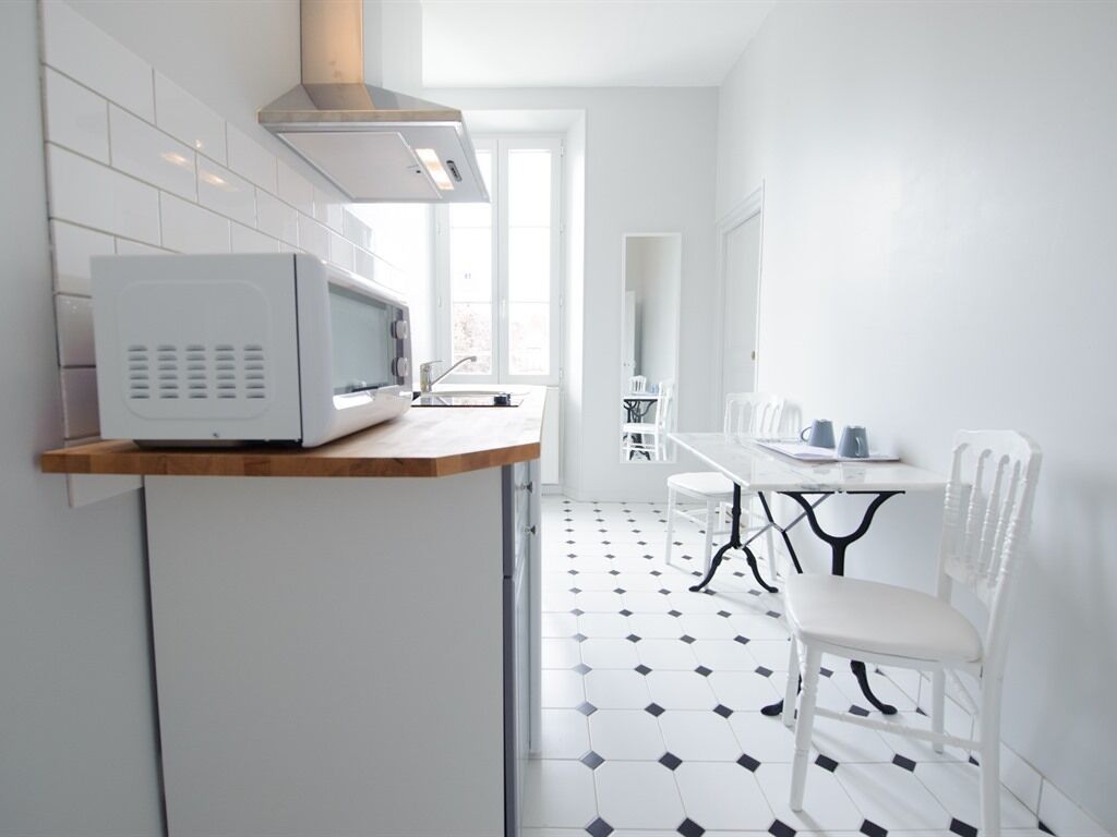 Una cocina moderna con un microondas sobre una encimera de madera, una mesa de comedor con sillas y un suelo con estampado blanco y negro.