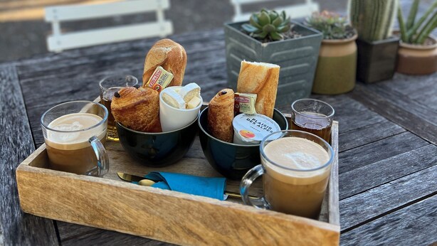 A wooden tray with food and drinks on an outdoor table.