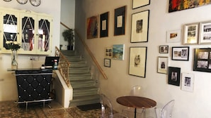 A cozy living area with a staircase, a black tufted sofa, clear plastic chairs, and a small wooden table. - Lee's House Bed & Breakfast Sliema (Sliema)