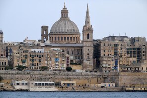 A coastal cityscape with historic buildings, a prominent dome, and a tall tower.
