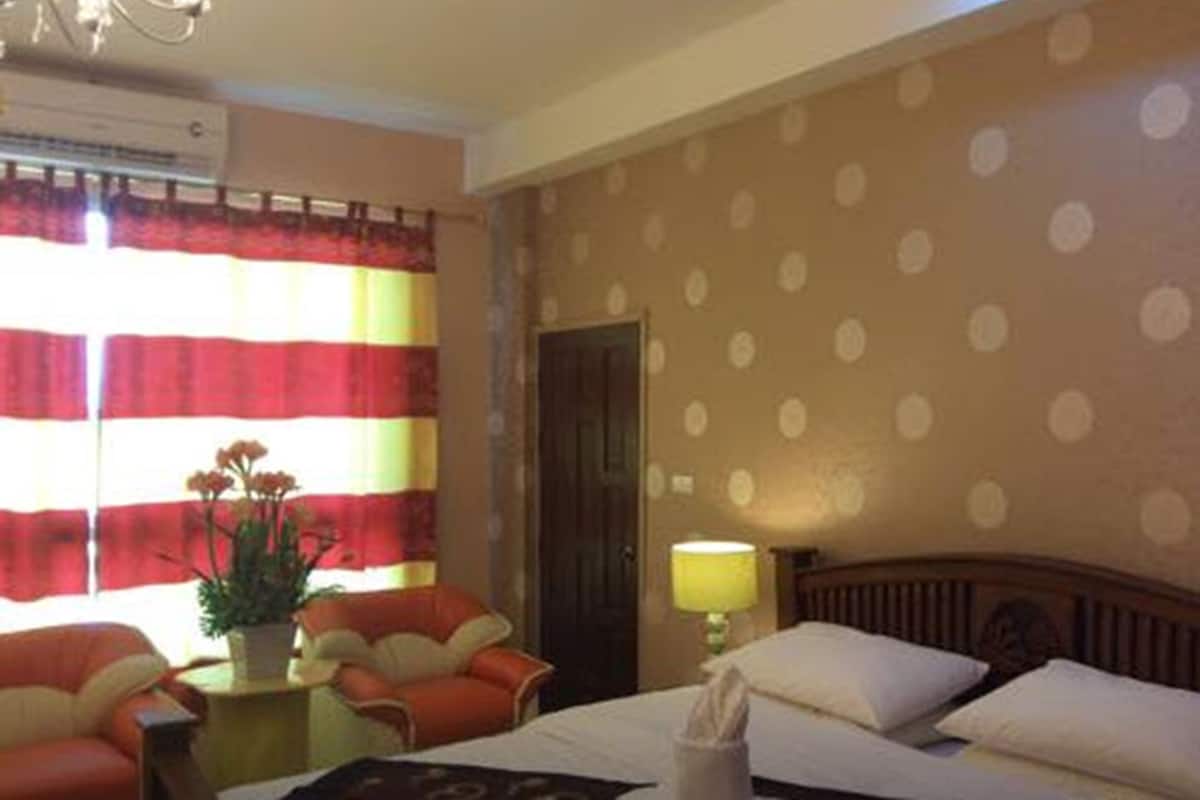 A hotel room with a bed, a nightstand, a lamp, a chair, and a window with curtains.