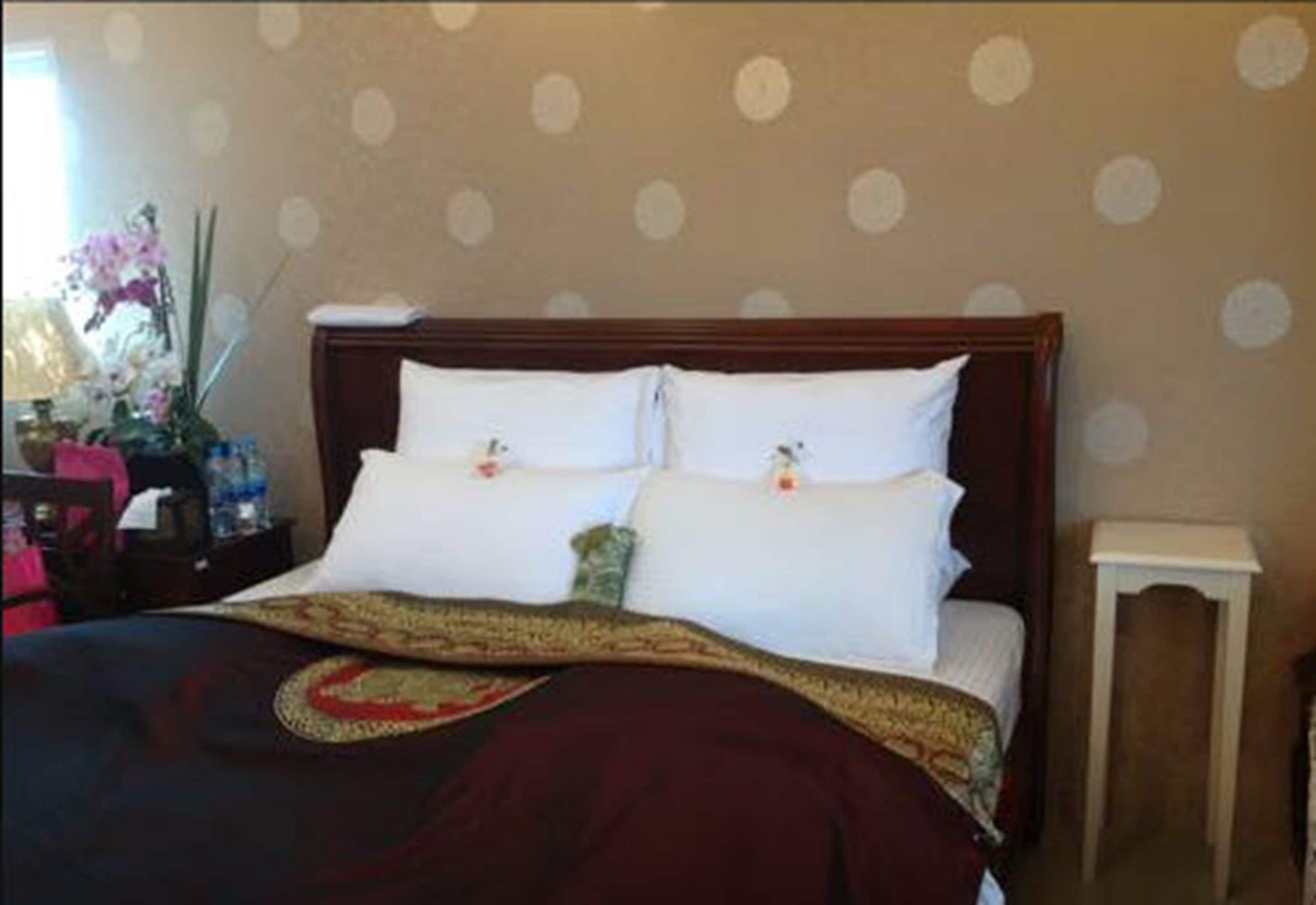A neatly made bed with a dark red blanket and a decorative pillow.