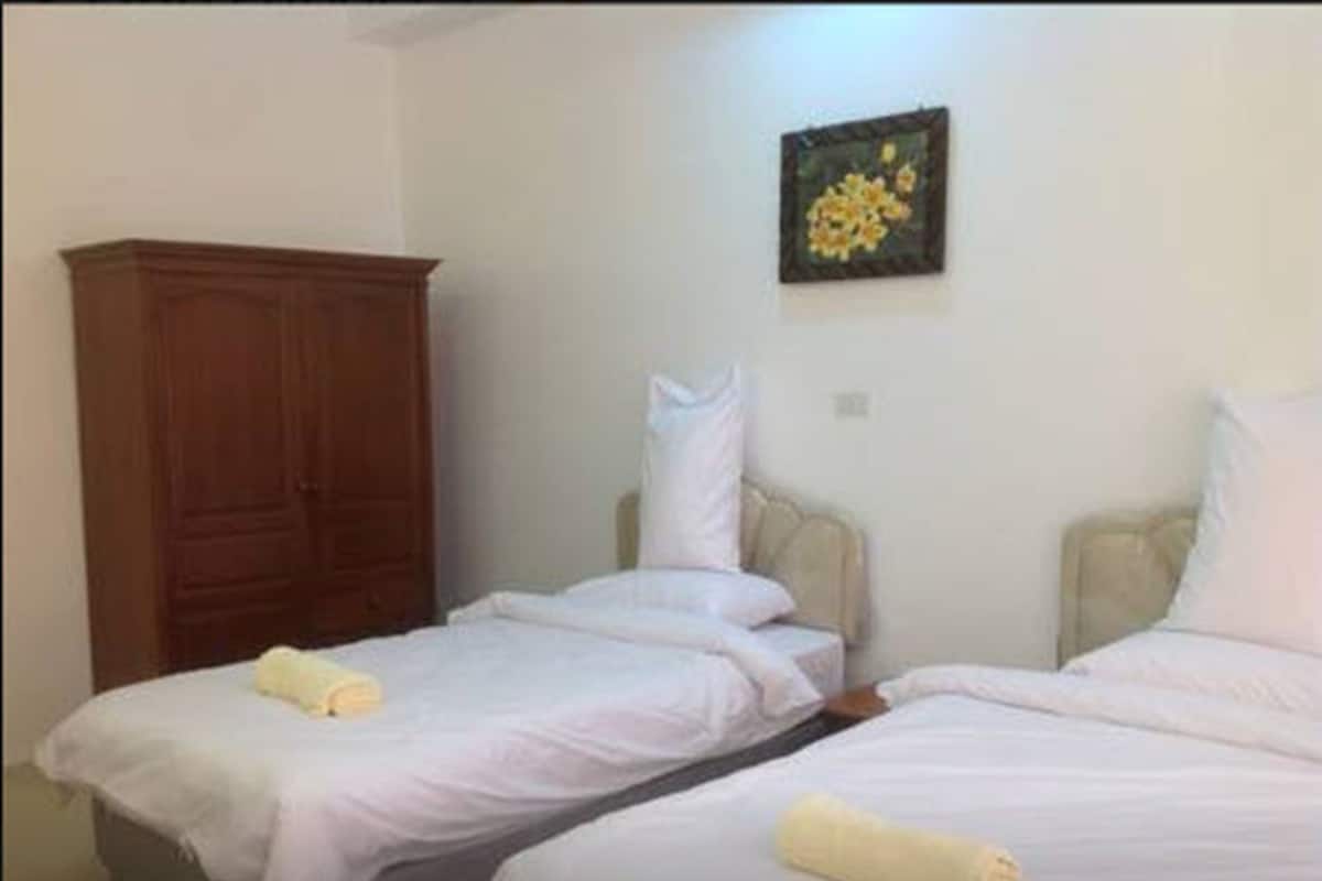 A hotel room with two beds, a wooden wardrobe, and a painting on the wall.