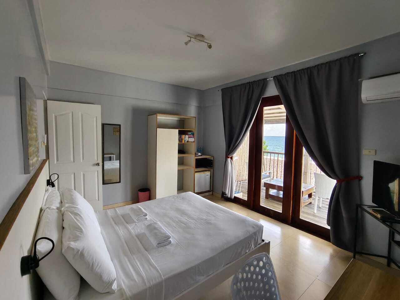 Habitación de hotel con cama, escritorio, televisión, armario y balcón con vista al mar.