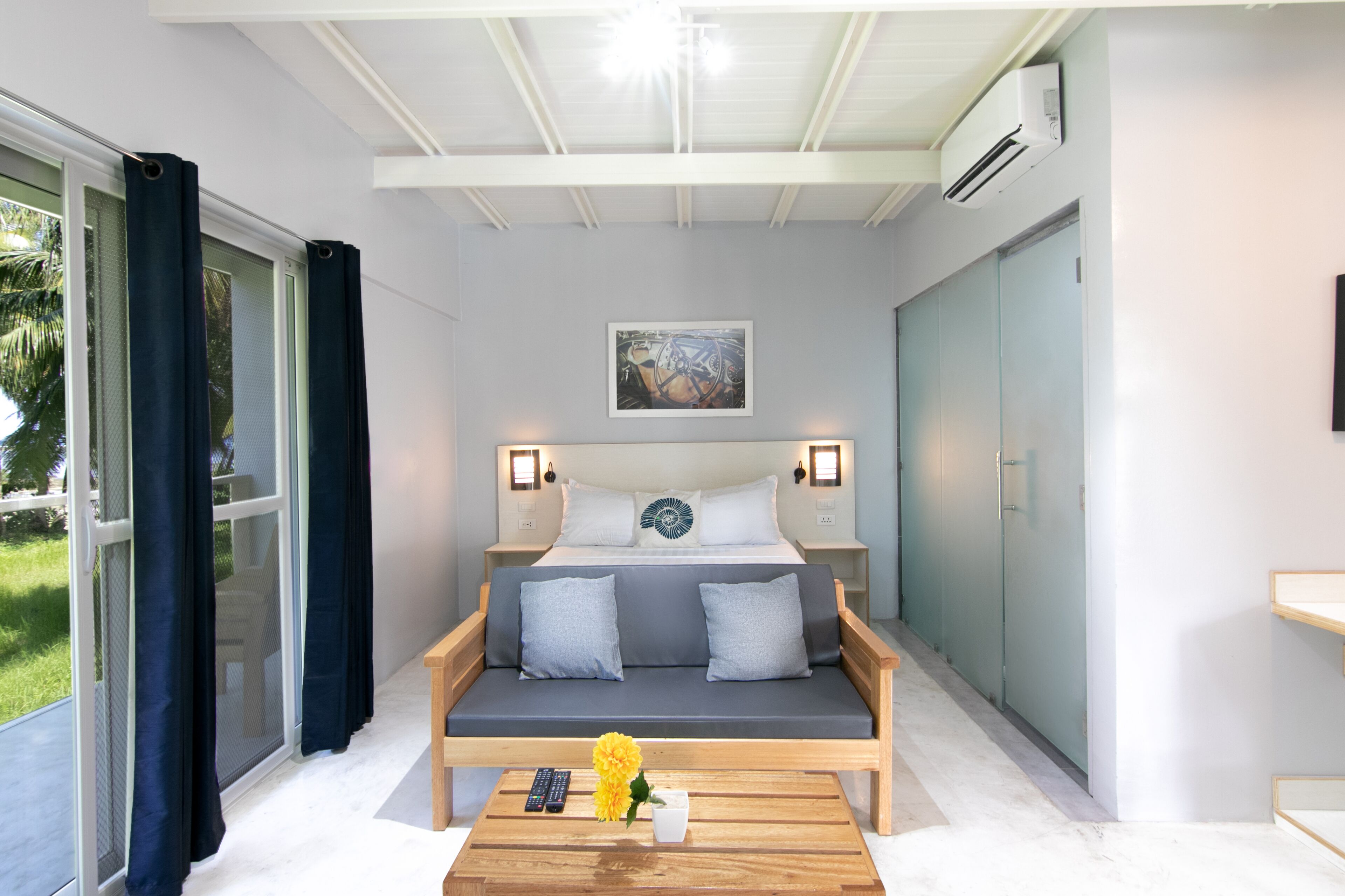A bedroom with a bed, bedside lamps, a painting, a sofa, and a coffee table with a remote and flowers.