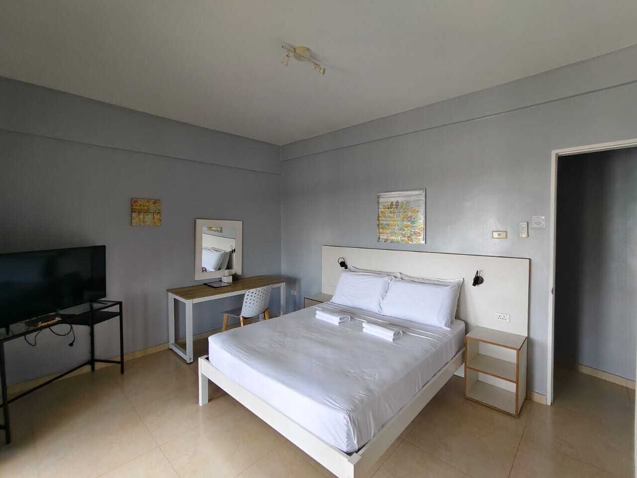 A bedroom with a bed, a desk, a television, and a door.