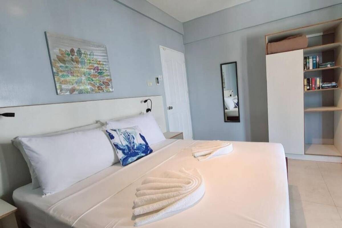 Habitación de hotel con cama, mesita de noche, armario, estantería y espejo.
