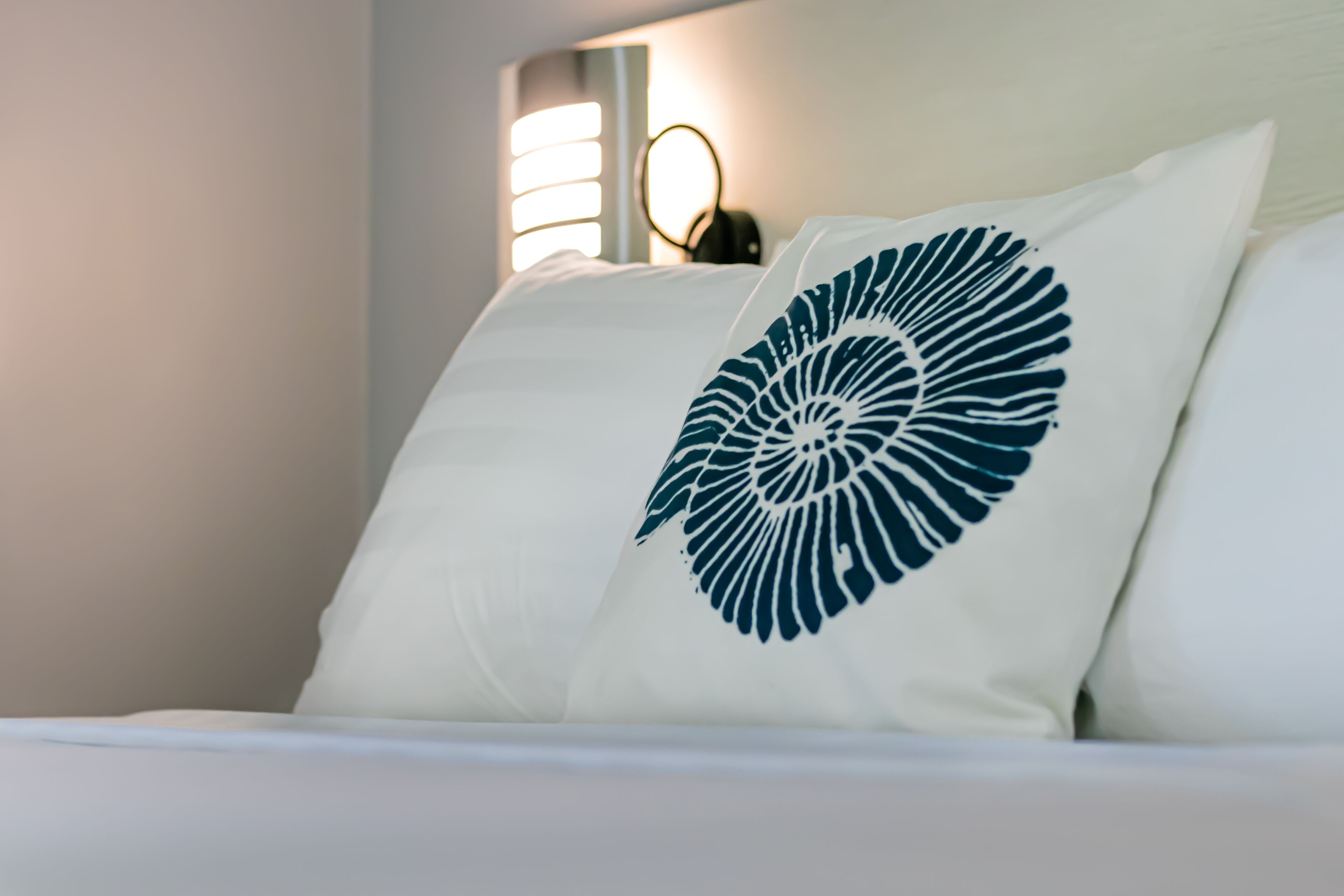 A bed with white bedding and a pillow featuring a blue leaf design.