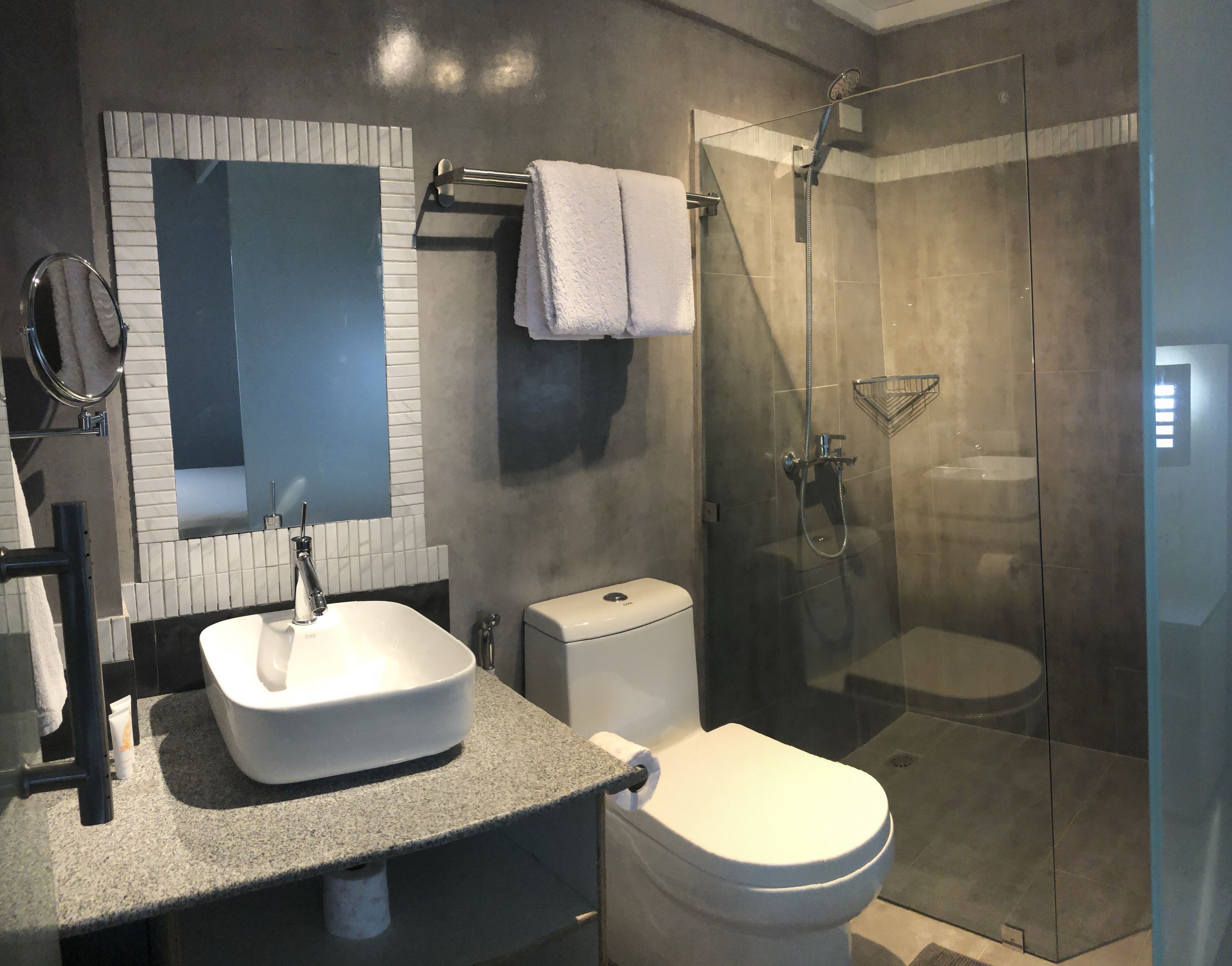 A modern bathroom with a granite countertop, a white sink, a toilet, and a glass-enclosed shower.