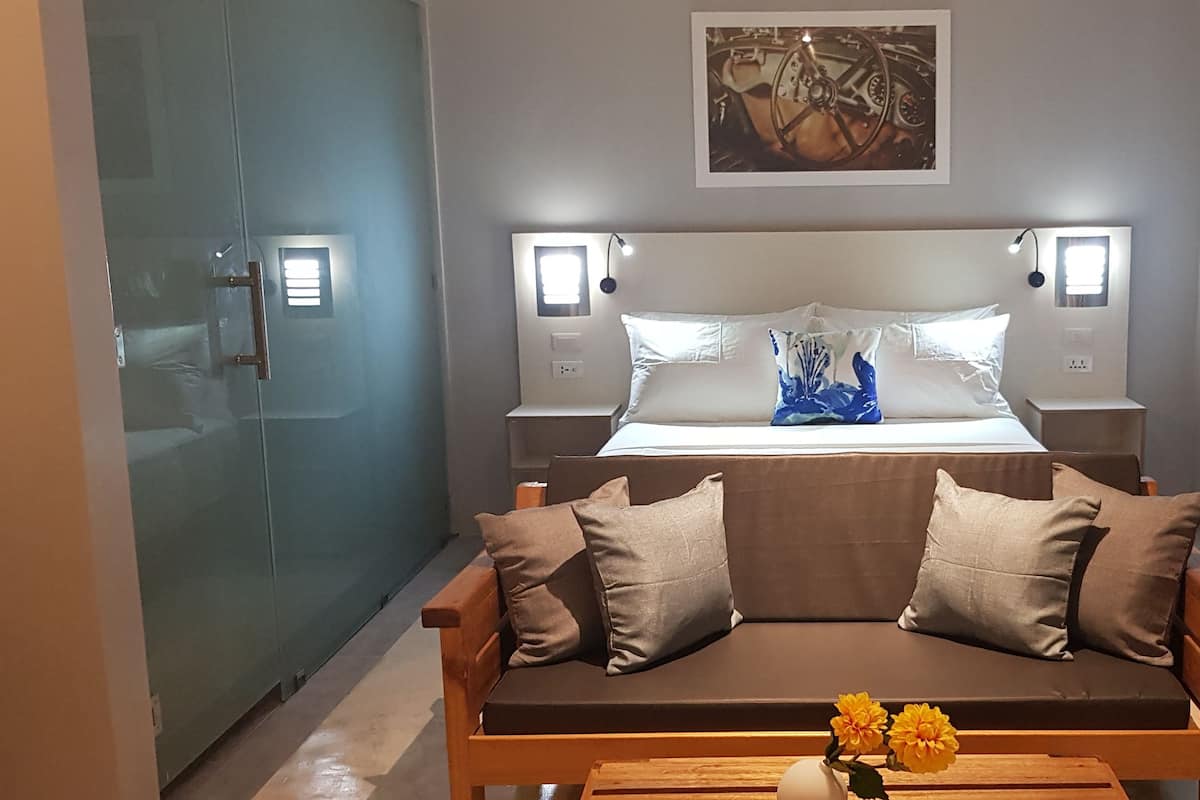 Una habitación de hotel moderna con una cama, lámparas de noche, un sofá y una obra de arte colgada en la pared.