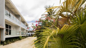 A modern building with a balcony, a pathway, and tropical plants. - Reef Beach Resort (General Luna)