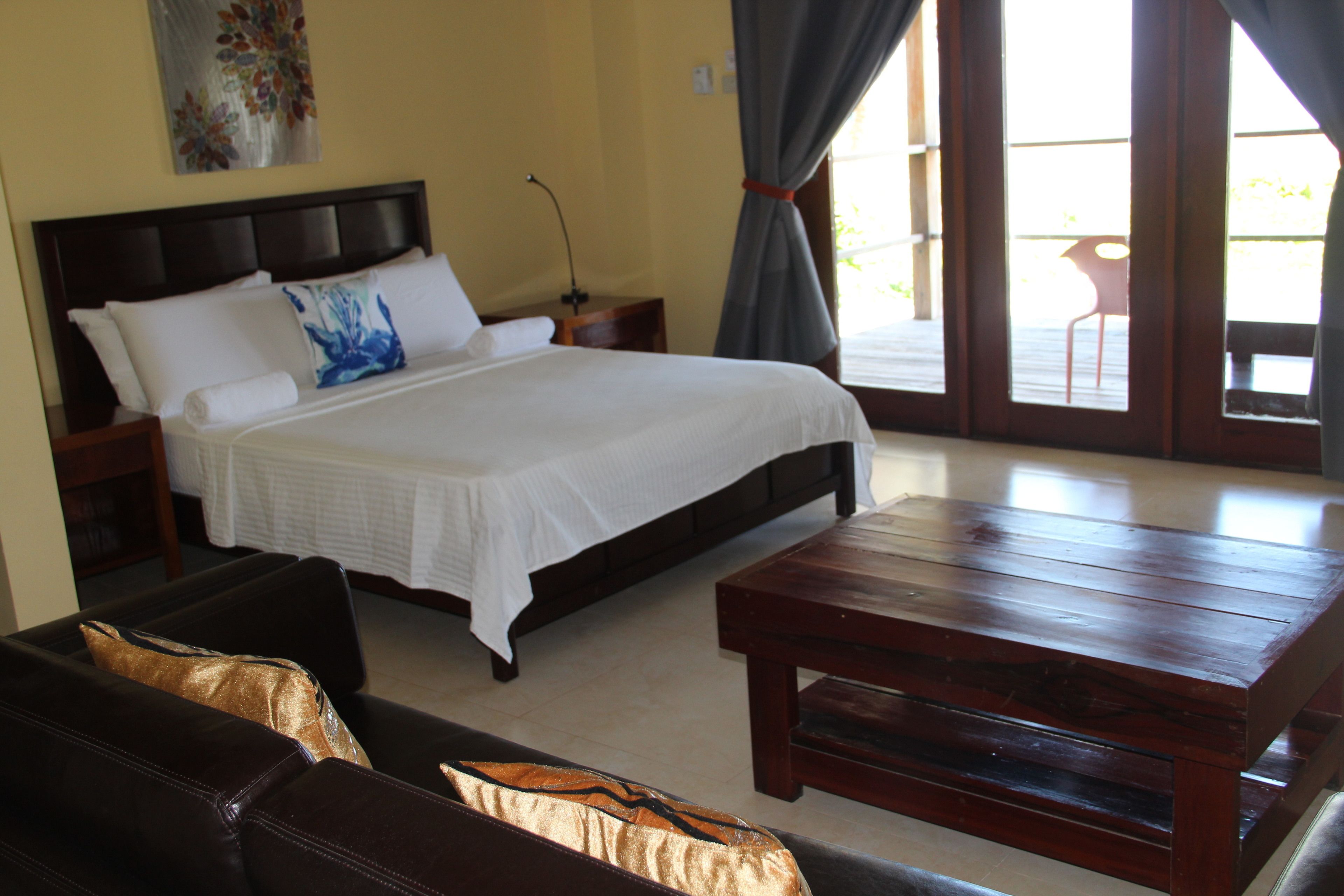 Une chambre à coucher comprenant un lit, une table de chevet en bois, une commode, un banc en bois et une vue sur l’extérieur.