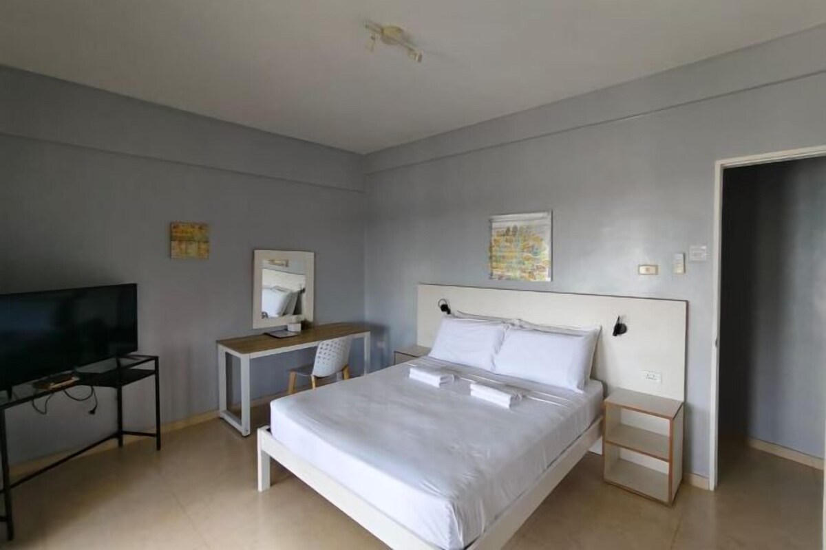 A modern bedroom with a bed, a desk, a chair, a television, and a door.