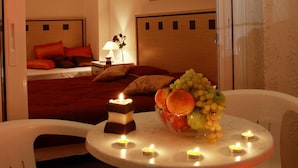 Ein Hotelzimmer mit Bett, Nachttisch mit Lampe, Obstschale und Kerzen auf einem kleinen Tisch.