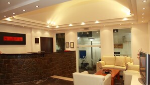 Eine moderne Lobby mit einem Stehpult an der Rezeption, einer Sitzecke mit einer Couch und Sesseln, einem Fernseher und gerahmten Zertifikaten an der Wand.