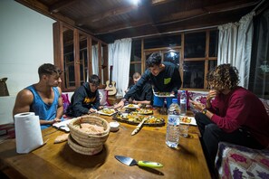A group of people dining at a wooden table with various dishes, a guitar, and a water bottle. - Original Surf Morocco - Hostel (Aourir)