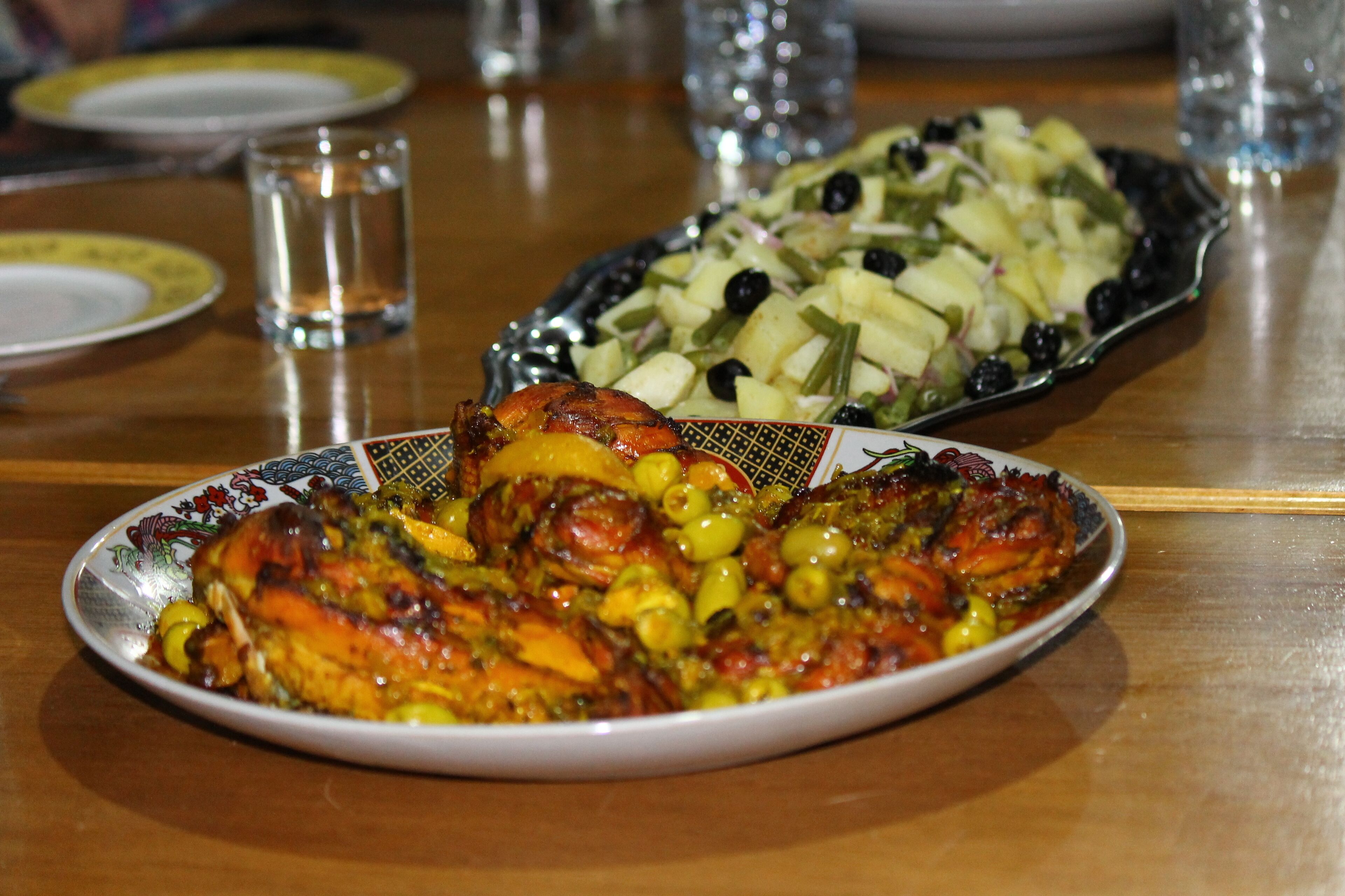 A dining table with a plate of roasted chicken and a side salad.