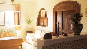 A cozy living room with a sofa, a small table, a potted plant, and a decorative wooden door. - Original Surf Morocco - Hostel (Aourir)