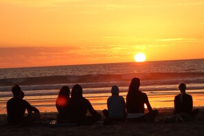 A sunset over the ocean with people sitting on the beach. - Original Surf Morocco - Hostel (Aourir)