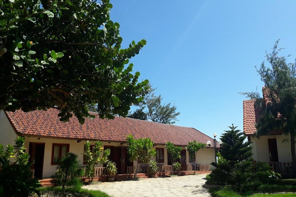 A courtyard with a tiled-roof building, surrounded by greenery and a paved walkway.