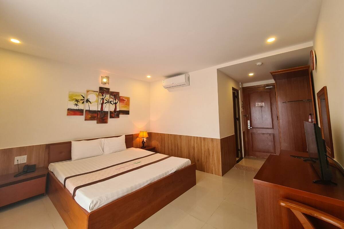 A hotel room with a large bed, a desk, a chair, and a wardrobe.