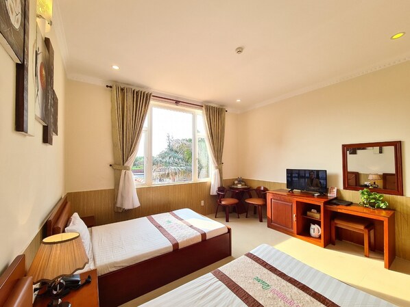 A hotel room with two beds, a desk with a chair, a television, and a window with curtains. - HaiDuong Intourco Resort (Vung Tau)