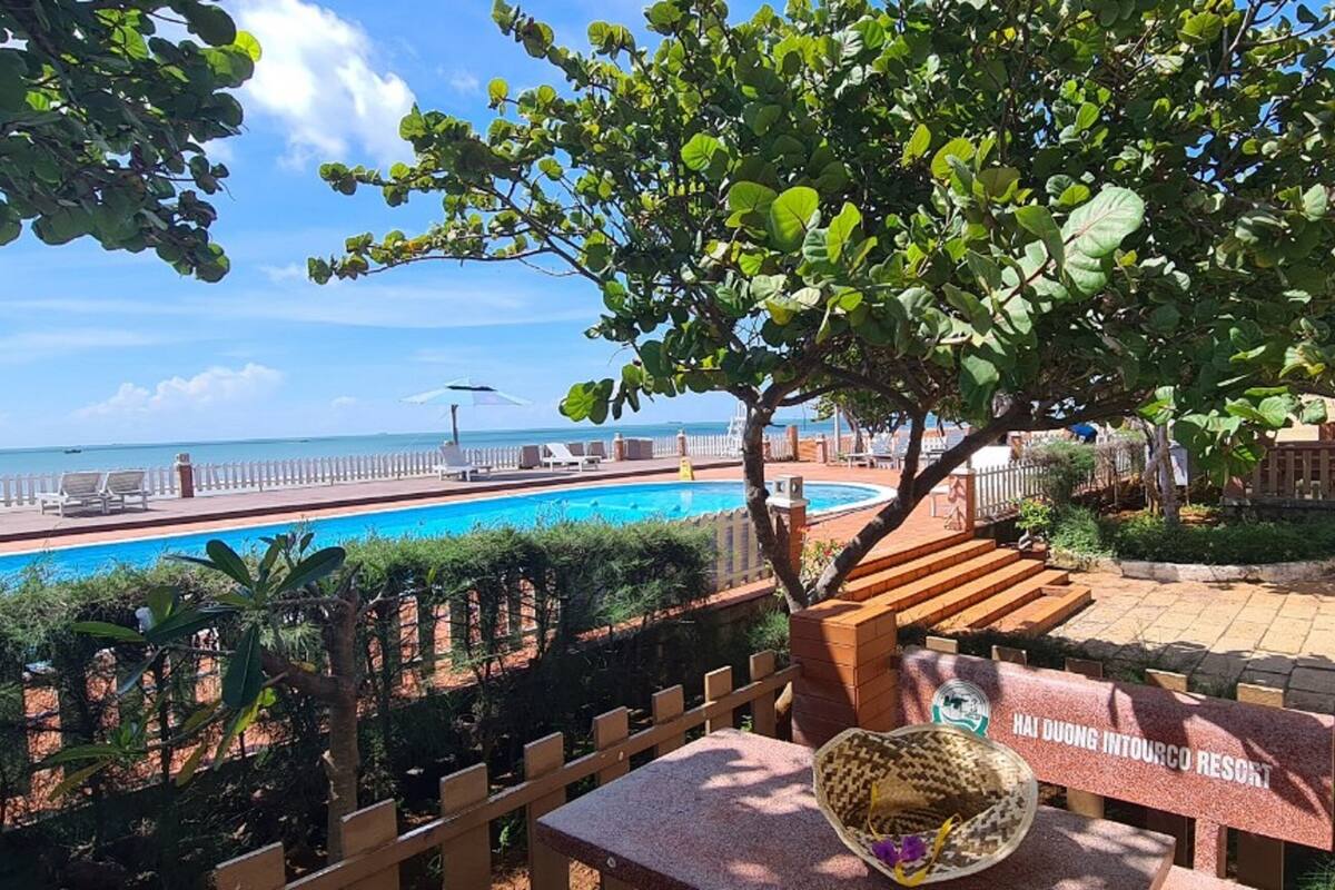 A poolside area with a view of the ocean, a wooden fence, and a sign for Hai Duong Intourco Resort.