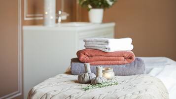 Ordentlich drapiertes Handtuchgestell auf einem Bett mit einer gemusterten Decke, einer kleinen Kerze und einem Rosmarinzweig.