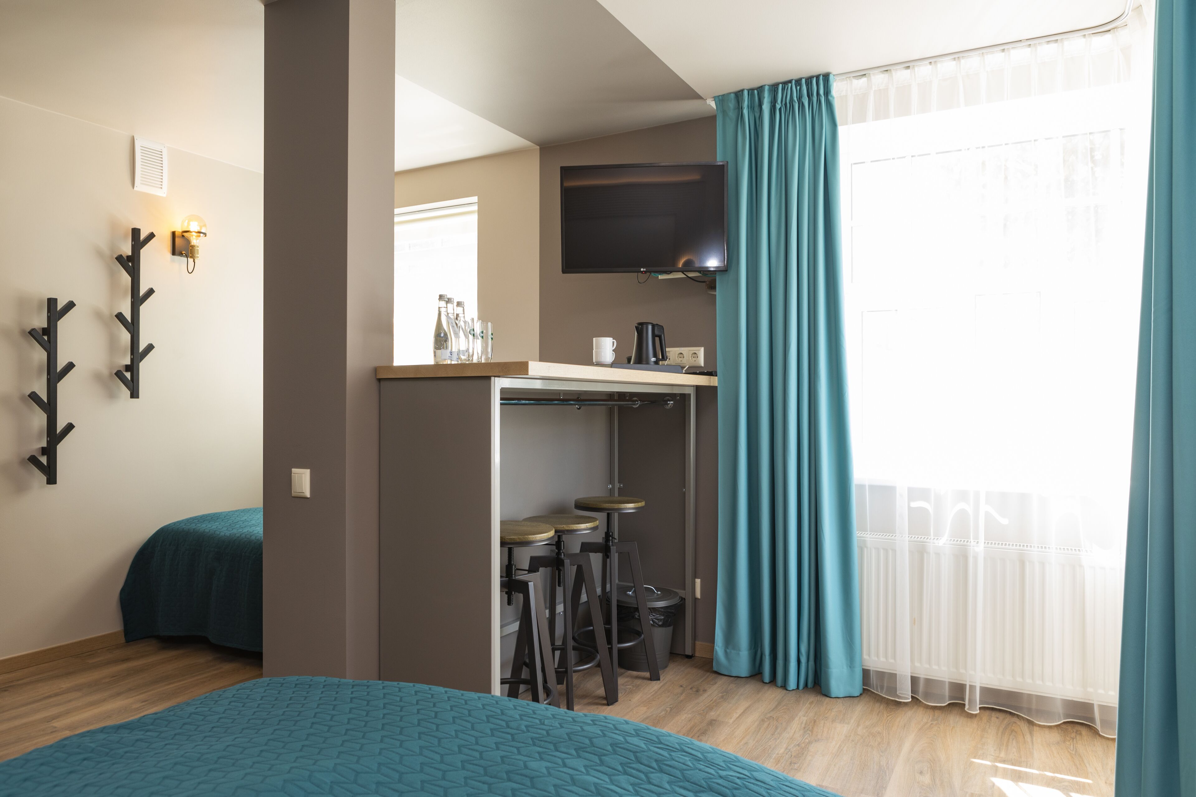 Una habitación compacta con cama, kitchenette pequeña, televisor y ventana con cortinas.