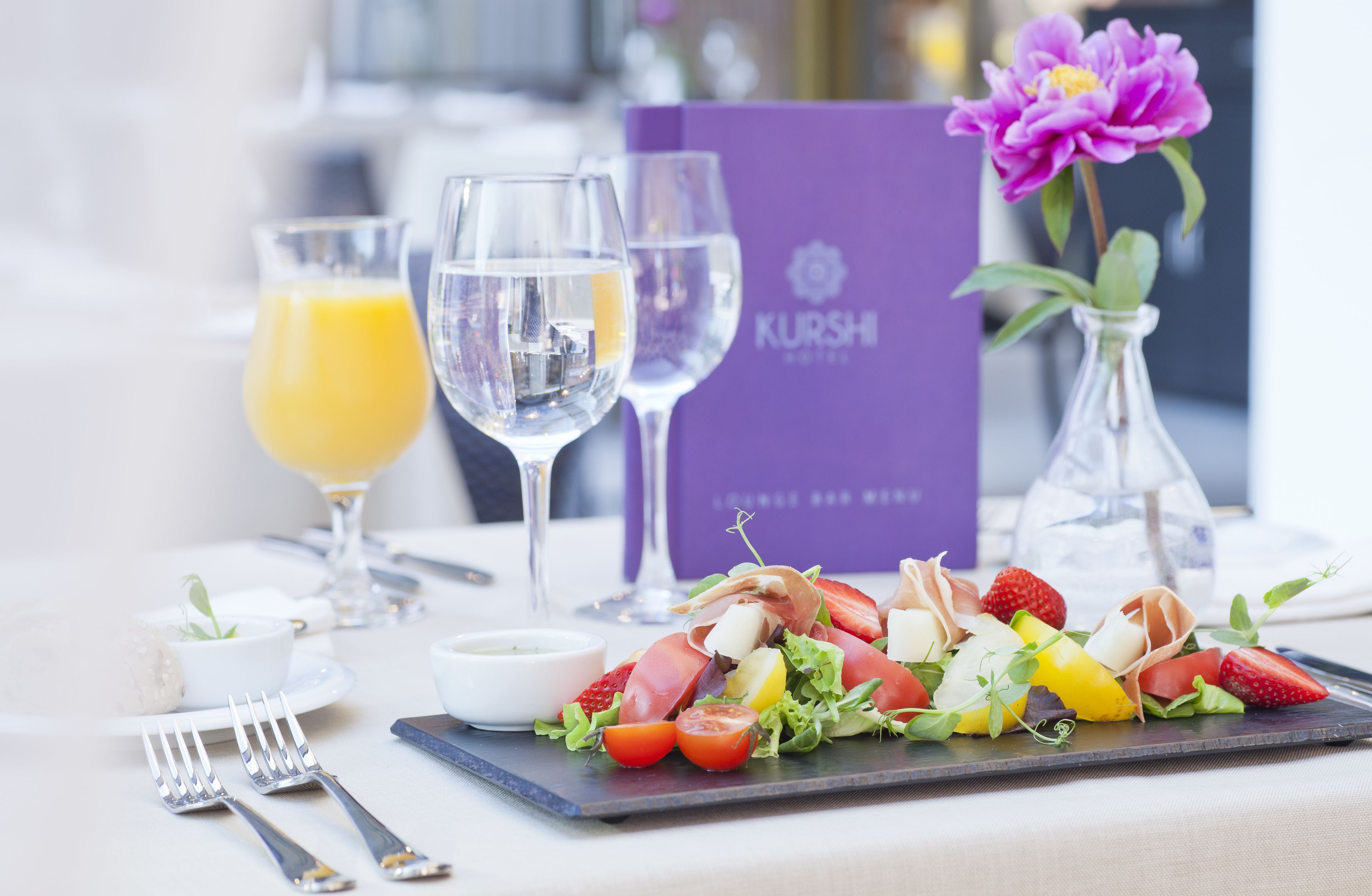 A dining table with a salad, two glasses of orange juice, and a purple menu.