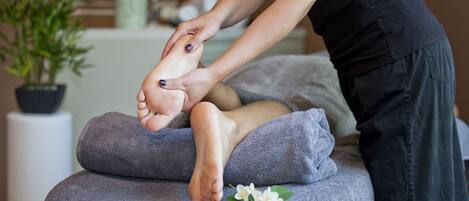 A foot massage being performed on a massage table with a towel and flowers.