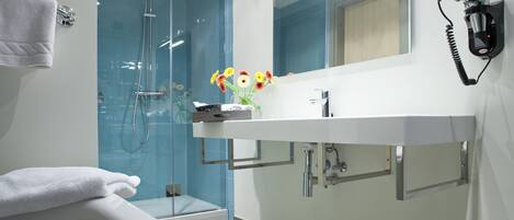 A modern bathroom with a glass-enclosed shower, a white sink with a mirror, and a towel rack.